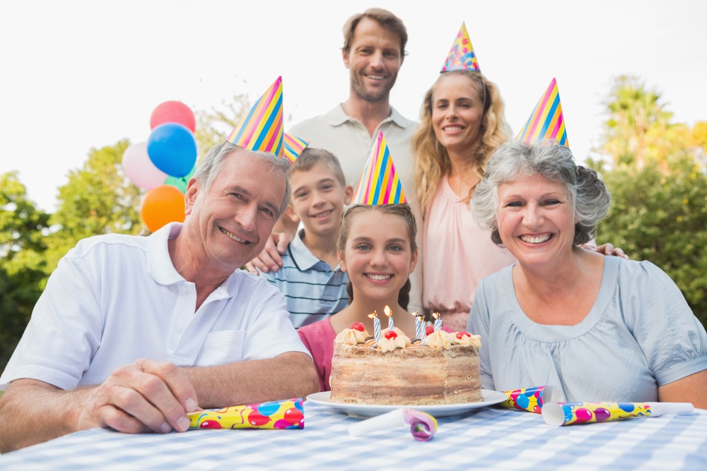 Cheerful family smiling at camera at birthday party outside at picnic table